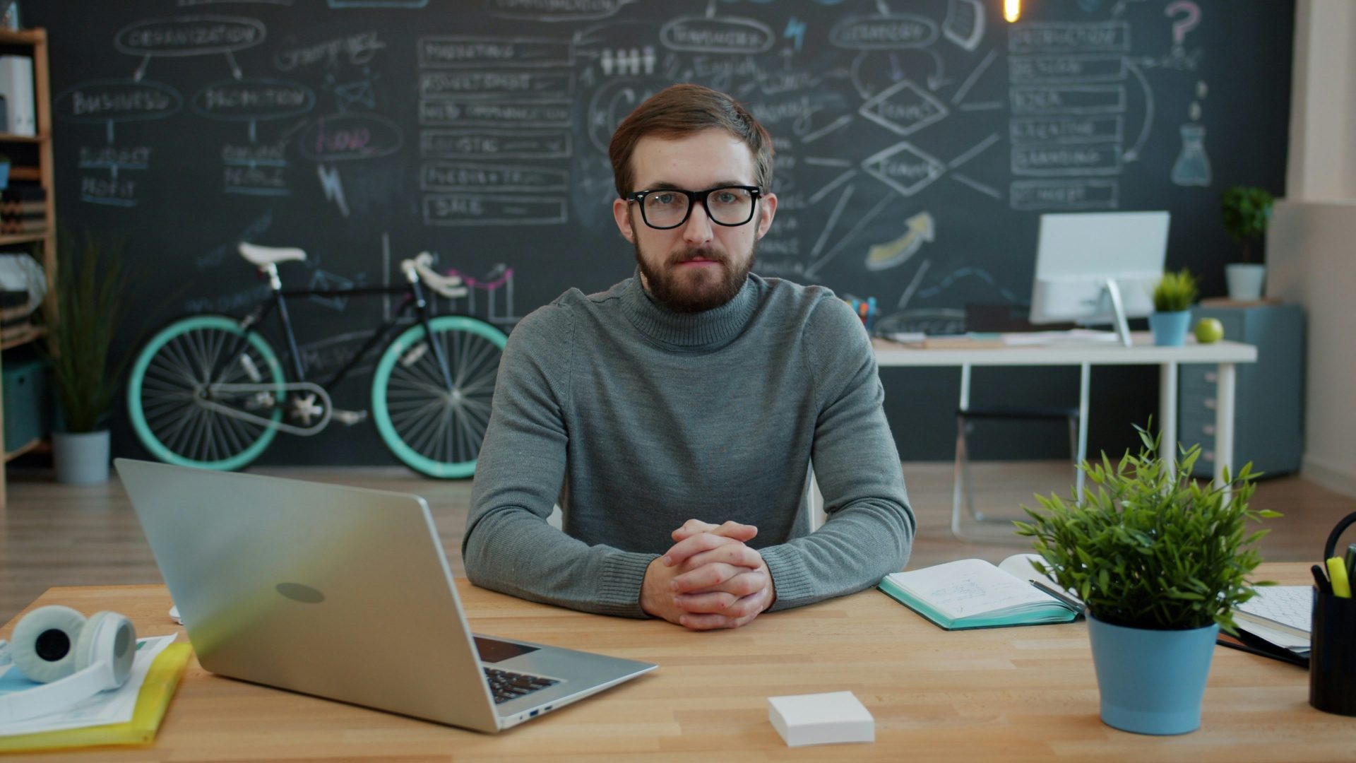 Man sitting at desk with laptop and bicycle behind him.